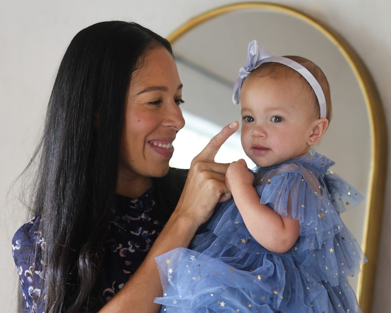 Woman holding a baby in front of a mirror, both wearing blue outfits.